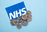 Money sits on a backdrop of the NHS logo