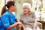 Nurse in blue uniform kneeling down next to older lady who is sat in an armchair