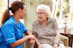 Nurse in blue uniform kneeling down next to older lady who is sat in an armchair