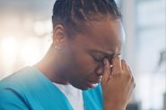 A Black female nurse looking upset with her hand on her head