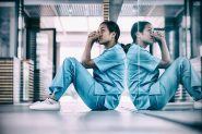 An Asian nurse sits on the floor in a hospital corridor looking worried